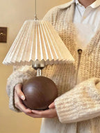 Person holding a decorative lamp with a pleated shade and wooden base.