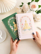 Hands holding spiral notebooks with meditation cover designs, surrounded by pale pink roses and a white cup