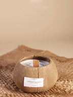Coconut shell candle with a wooden wick on a woven mat against a beige background