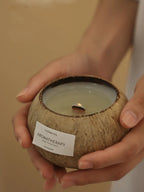 Coconut shell candle with a label held by hands against a neutral background