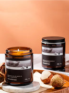 Two candles with labels on a wooden surface against a peach-colored background