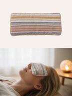 Yellow and multi-colored striped fabric herbal gravity eye pillow: top view of the product and a woman using it for relaxation in a cozy bedroom (with a glowing lamp in the background), intended for eye comfort and sleep support