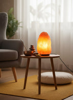 Salt lamp on a wooden side table in a living room setting with a plant and cushion.