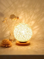 Decorative lamp with wicker design on a wooden base, surrounded by dried flowers on a soft background.