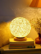 Woven ball lamp on books with a warm glow in a cozy room setting