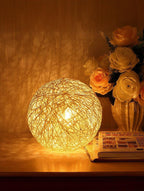 Woven ball light on a table with flowers and a magazine in the background