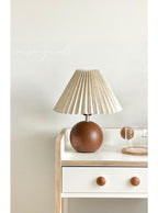Table lamp with pleated shade on a wooden side table against a light wall.