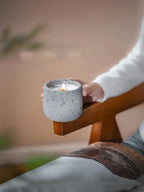 Person holding a small concrete candle holder with a lit candle outdoors.